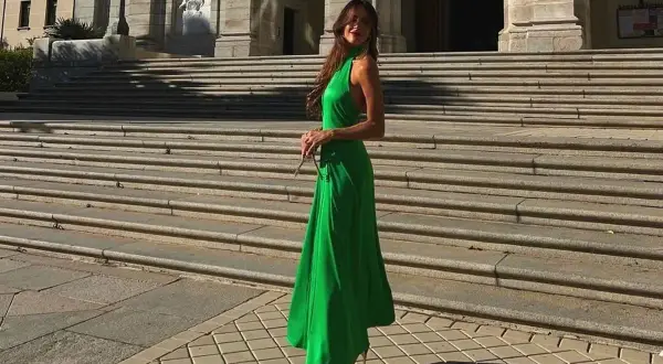 Mujer con vestido verde largo y sandalias plateadas posando en escalinatas de piedra.